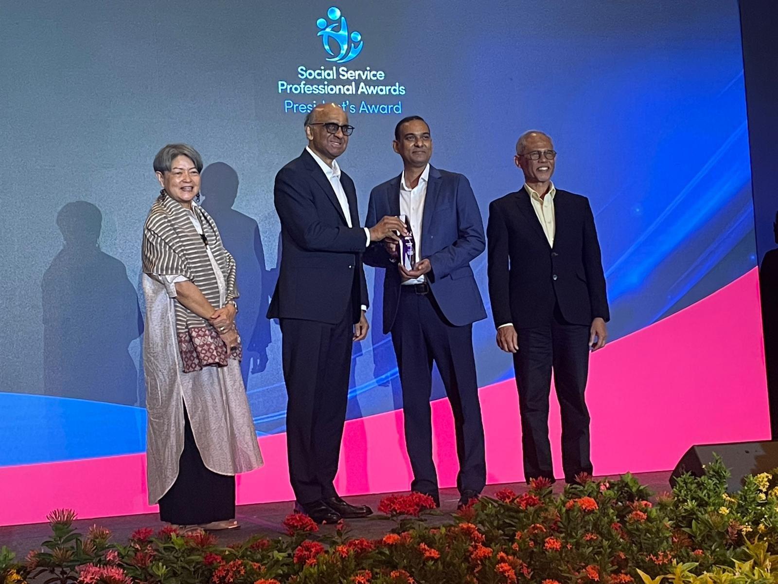 4 people standing on a stage, 1 woman, 3 men awarding ceremony at social service professional awards president's award