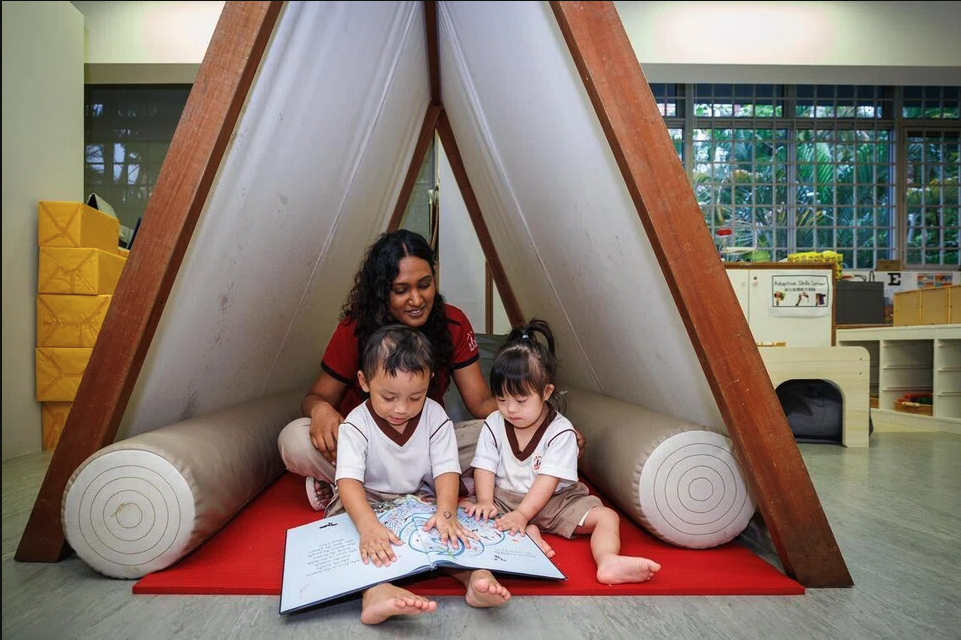 Teacher reading a book with two children at the calming down tent